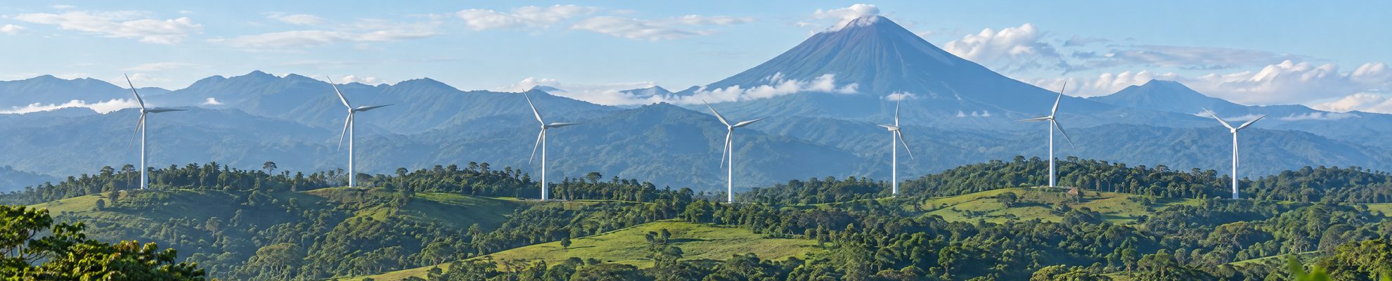 Wind turbines on green ridges in Costa Rica with a volcano behind them, part of the 98.6 percent renewable grid